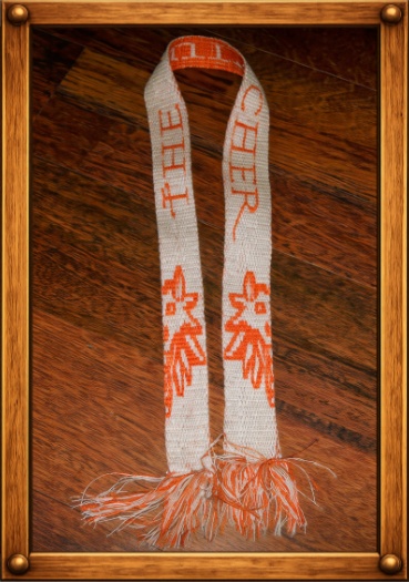 Handgewebtes Band in Naturweiß und Orange mit der Aufschrift „THE WITCHER“, Wolfskopf und Fransen an den Enden.