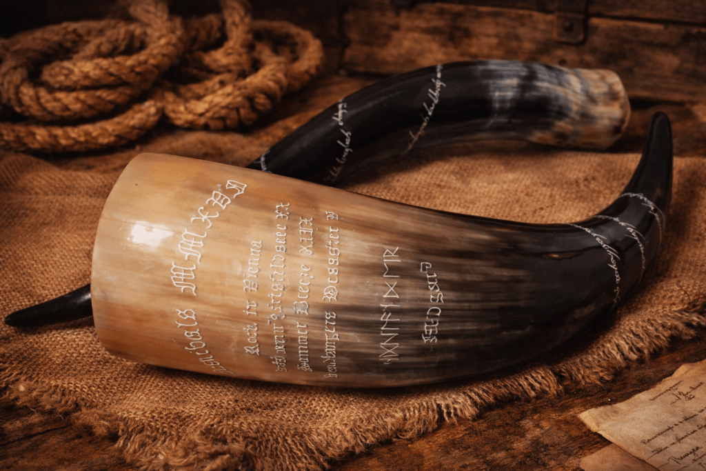 Handgraviertes Trinkhorn mit weißer Runenschrift und nordischer Inschrift, auf rustikalem Stoff und Holzuntergrund präsentiert.