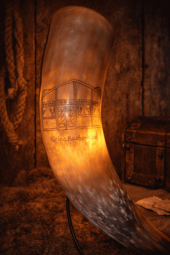 Lampe aus einem gravierten Trinkhorn, von innen warm beleuchtet, mit Darstellung einer Hausfassade und der Aufschrift „Kleine KüchenKiste“
