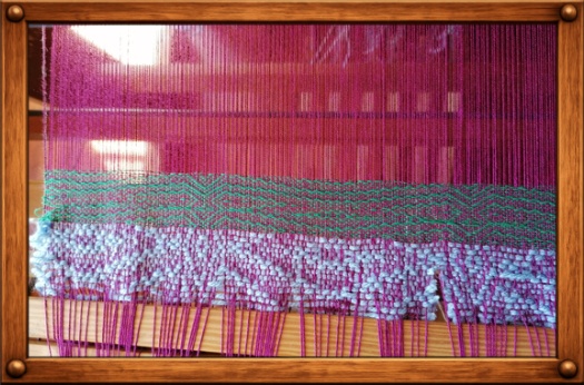 Detailaufnahme eines Webstuhls mit pinken Fäden und bereits gewebtem Stoff.