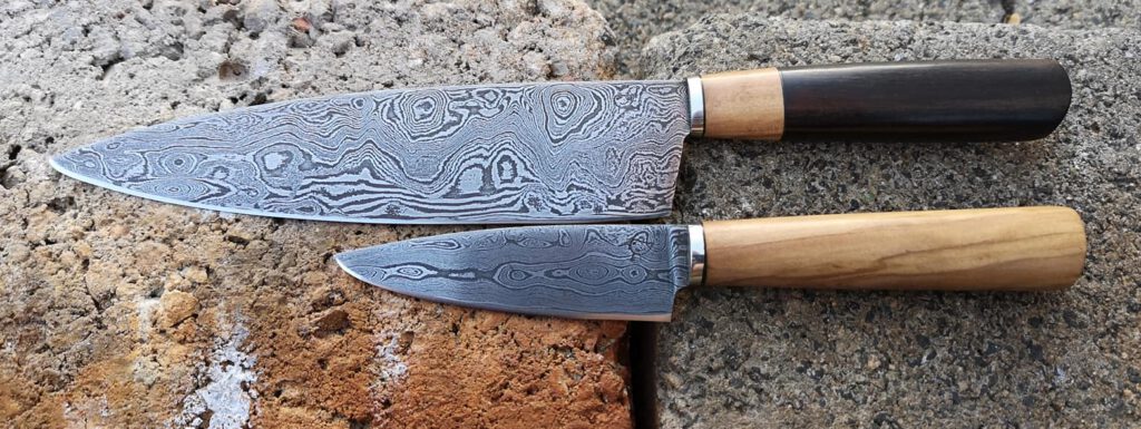 Zwei Damastmesser mit Holzgriffen auf rauer Steinoberfläche.