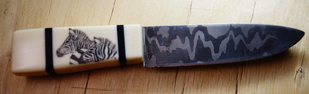Messer mit Zebramotiv im Griff und dunkler Klinge auf Holz.