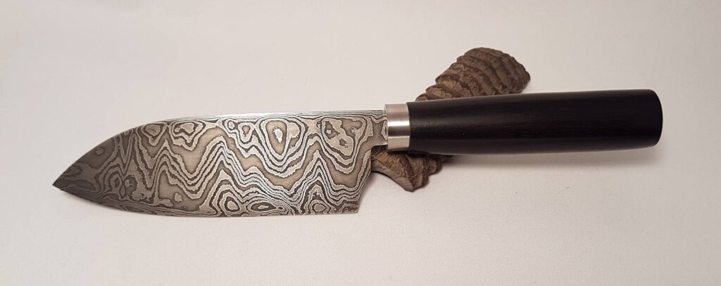 Kompaktes Damastmesser mit dunklem Griff vor hellem Hintergrund.